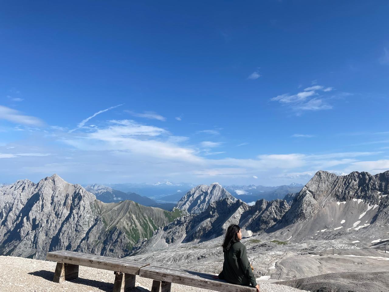 Elizabeth sitting at a mountain overlook, facing the alpine landscape.
